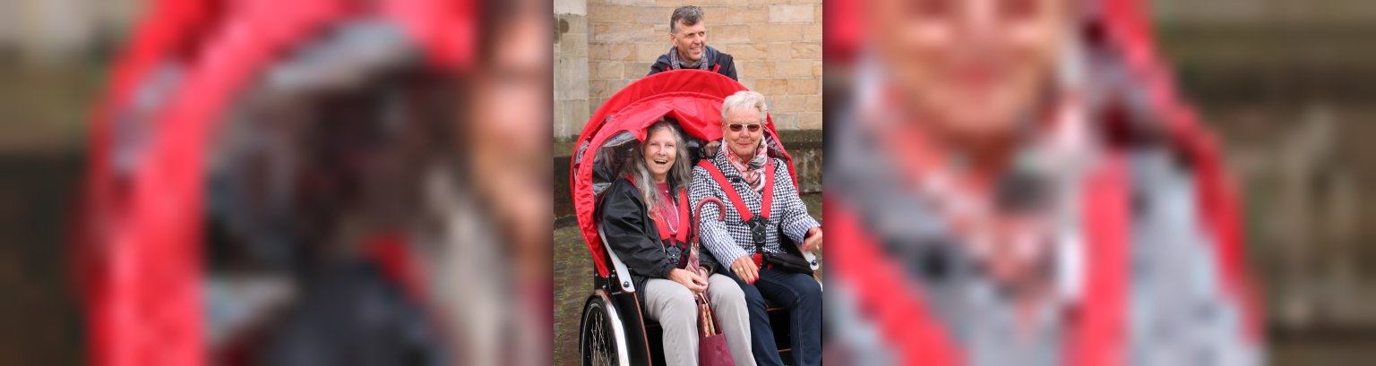 zwei Frauen sitzen in einer Rikscha - im Hintergrund ist ein Mann - alle lachen und sind fröhlich