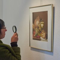 Eine Dame betrachtet ein Gemälde, sie hält eine Lupe in der rechten Hand
